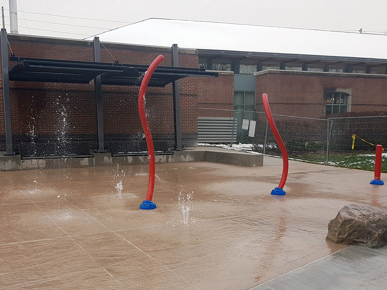 New splash pad being tested prior to opening. Image shows red vertical spray features and ground geysers shooting water.