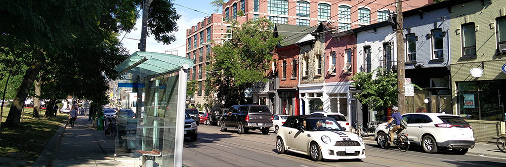 Painted two-storey buildings form a continuous row on the south side of Queen Street across from Trinity Bellwoods Park