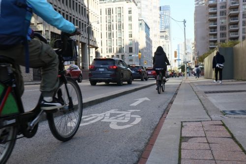Two people cycling in a cycle track on Wellesley Street, near Bay Street.