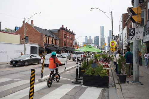 Woman on a folding bike is travelling south on Yonge Street and riding beside a curbside patio.