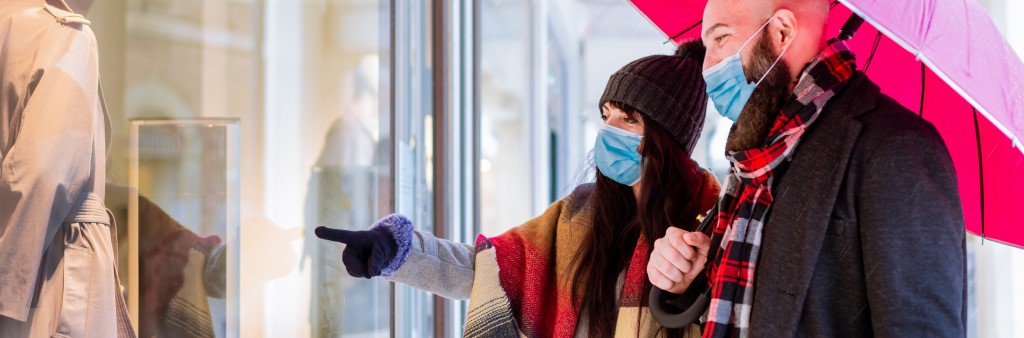 Two people holding an umbrella and window shopping while wearing surgical masks