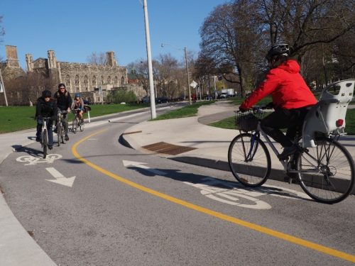 A group of people cycling one way in a cycle track, while a person cycling with a child bike seat going in the opposite direction.