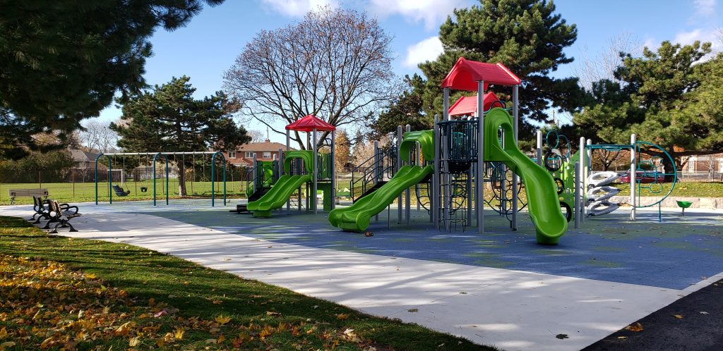 New play equipment at Roywood Park features junior and senior play structures with green plastic slides, an accessible swing set, and other climbing structures on a rubber play surface.