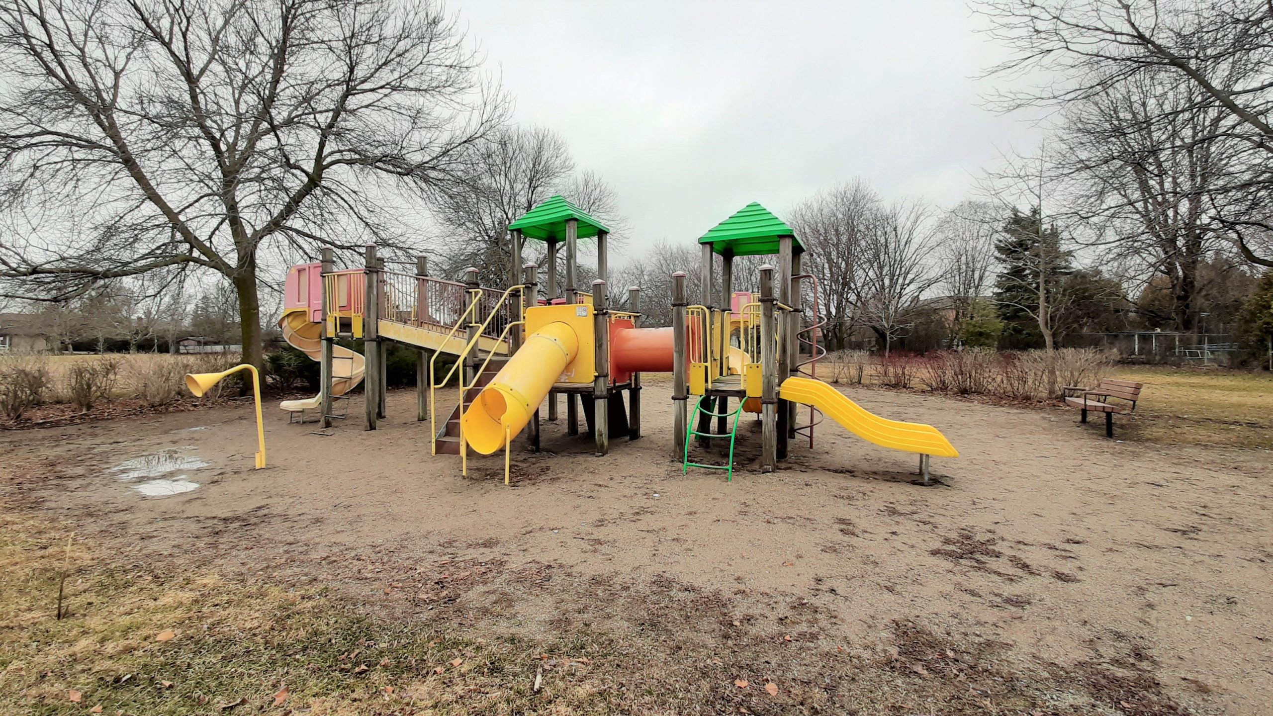 Old wood and plastic playground equipment, including three yellow slides of various sizes, on a sandy play surface.