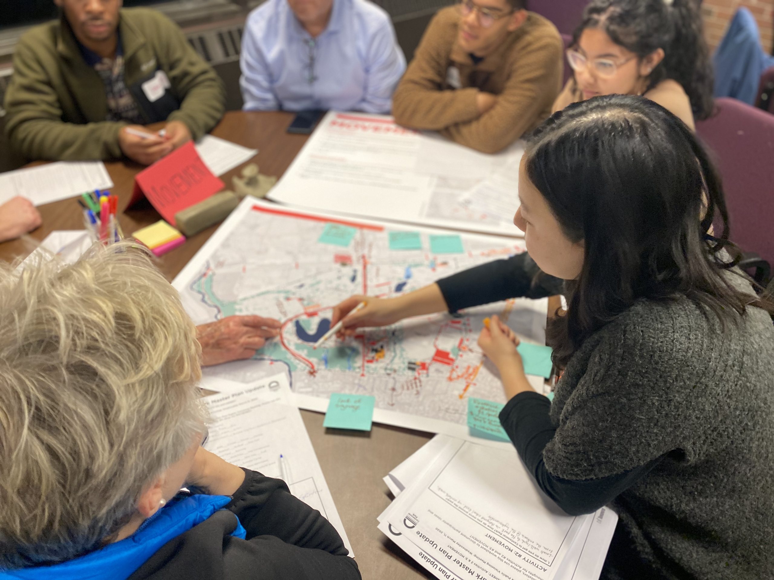 Workshop participants sit around a table discuss a map of Centennial Park, pointing to park features and adding ideas to sticky notes.