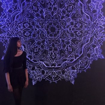 2022 Nuit Connects artist, Whyishnave Suthagar, standing in front of one of her artworks.