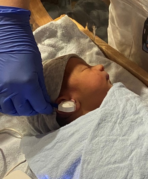 A sleeping newborn baby receiving a newborn hearing screen without sticker electrodes.