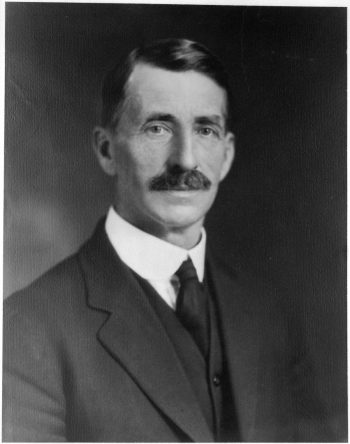 Black and white head and shoulder portrait of a man in a suit.