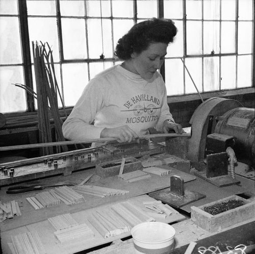 Woman working at a sanding machine wearing sweatshirt that says De Havilland Mosquito.