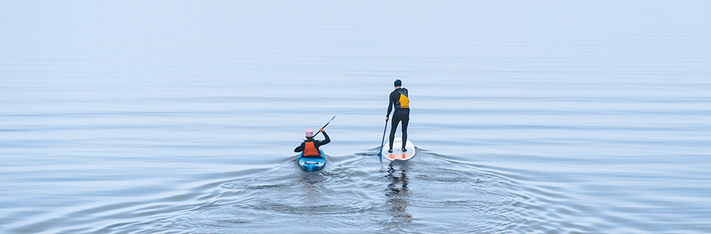 This is a photo two paddlers paddling in the lake. One is in a kayak and another in on a stand-up paddleboard.