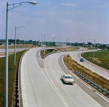 Colour view of highway 401 on ramp with three curving lanes, white car in the middle lane. 