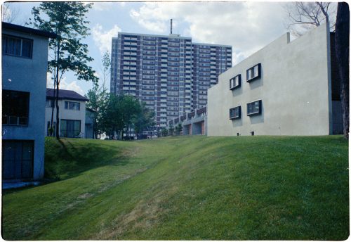 Colour view of high rise apartment building with grass and smaller buldings in foreground.