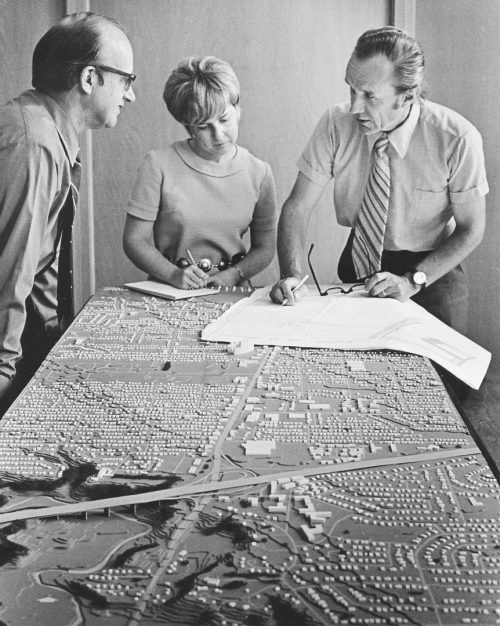 Two men and a woman looking at plans and a building model