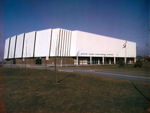 View of a large white building with flagpole and grass in foreground.