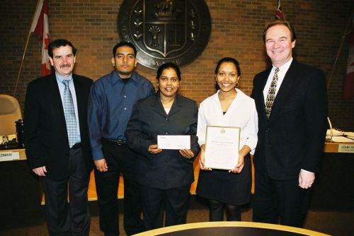 Group portrait of two women and three men. One woman holds a plaque and the other holds a cheque.