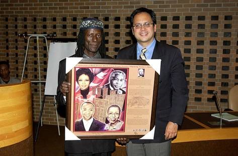 Colour image of two men holding a framed poster.