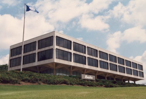 Colour exterior view of a three story commercial building with Bata sign and flag pole in front. 