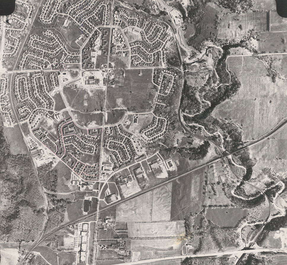 Aerial view showing Don Mills housing subdivision with curving roads and residential cul-de-sacs. Natural features are also visible including fields, trees and a river.