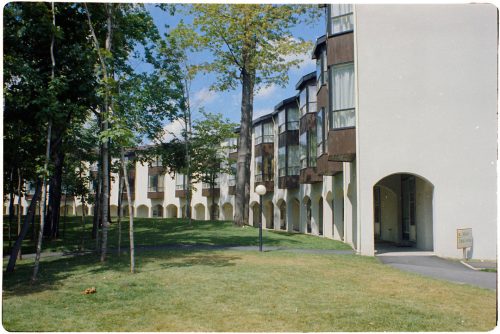 Colour view of two story townhomes in a curving pattern with trees in front.