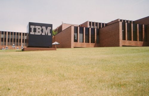 Colour exterior view of commercial brick building with large IBM sign and grass in foreground. 