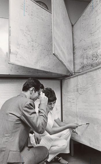 Man and a woman looking at a map mounted on a wall. Woman points to the map with a pen.