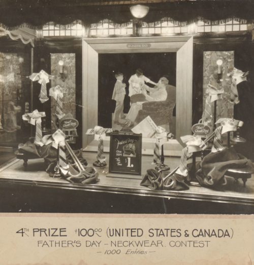 Store window display of ties, with an illustration of a father being pleased to receive a tie from two children. A sign says "give him a tie or two, $1."