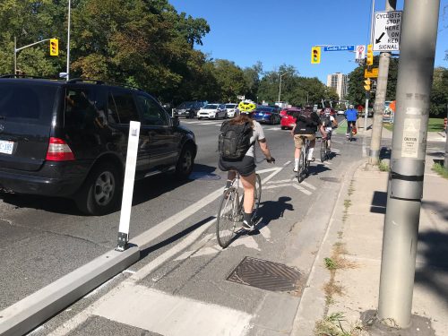 People on bikes approach an intersection in a cycle track that is protected from motor vehicle traffic with curbs and bollards