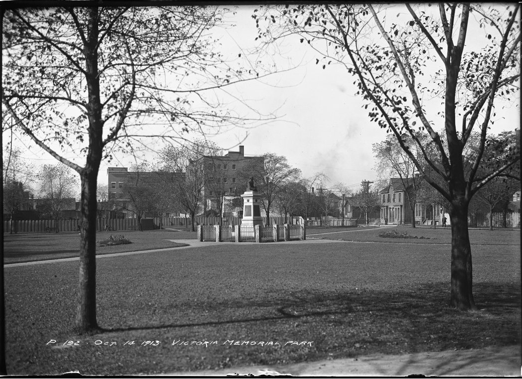 Photograph of Victoria Memorial Square in 1913 looking northwest from Portland Street to the corner of Bathurst and Wellington Streets. Image depicts a statue in the centre of the square crossed by pathways intersecting the park.