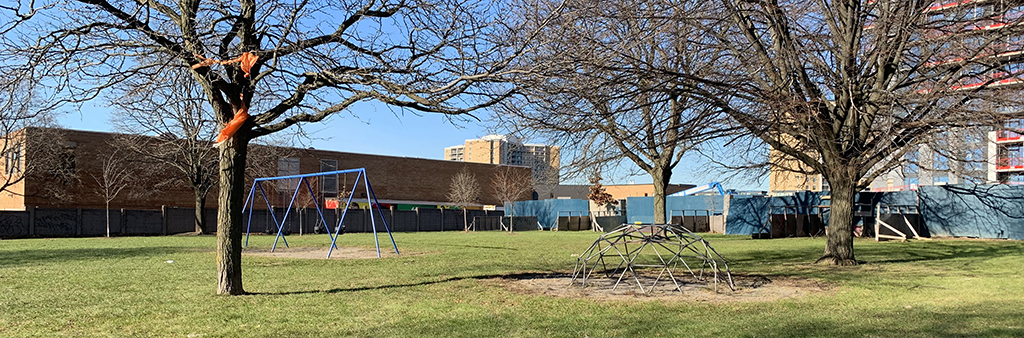 A photograph of Warrender Park, with the playground in the foreground. The playground includes a domed climbing structure and a blue swingset. Grass surrounds the playground.