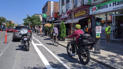 Two people cycle in a cycle track beside motor vehicle traffic