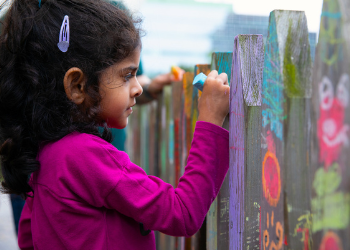 A young girl paints a fence