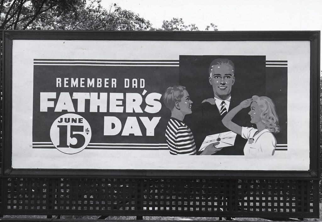 A billboard showing a white boy and girl giving a gift to a white man. The text says "Remember Dad, Father's Day, June 15th."