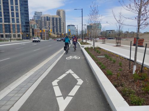 Two people cycle in a raised cycle track that is separate from motor vehicle traffic.