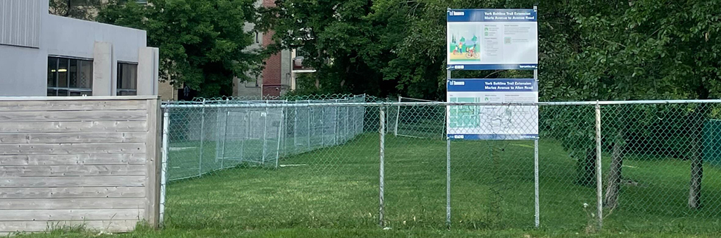 View of the future site of the York Beltline Trail Extension from Marlee Avenue. Lawn and trees are fenced off from the street and neighbouring buildings.