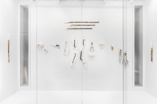 Glass display case with an arrangement of white artifacts or art pieces on a white background