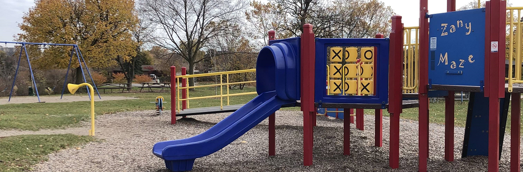 A blue, yellow and red playground, with a slide in the foreground and a swingset in the background.