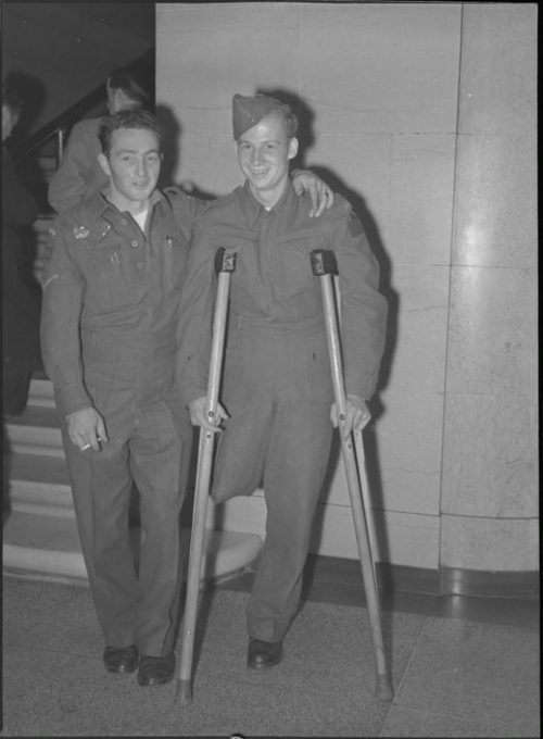 A black and white photo of two soldiers posing at Union Station both are returning from Dieppe and one soldier uses crutches due to an amputated leg.