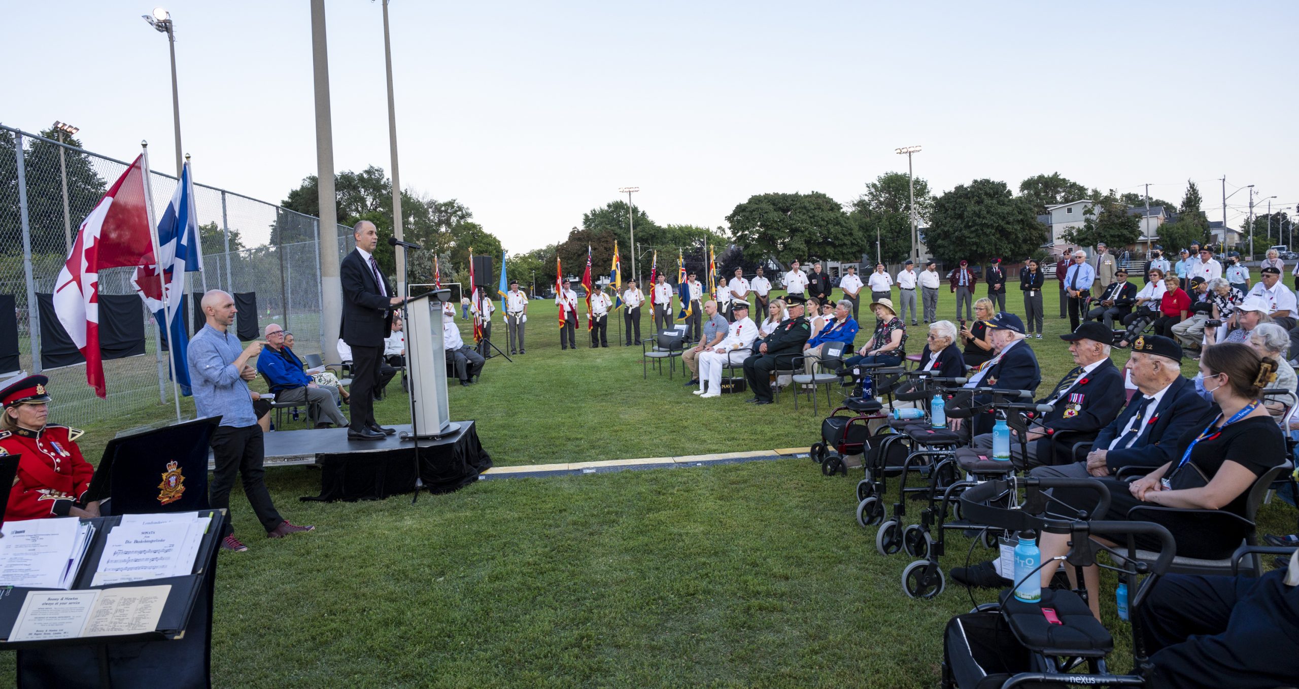 A crowd, including veterans, colour guards and guests, on the lawn of the Dieppe Park listening to the Deputy Mayor