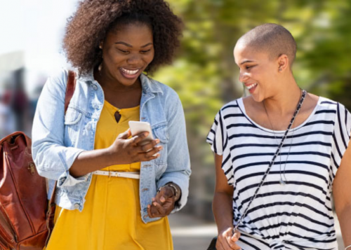 Two women walking together and looking at a mobile phone