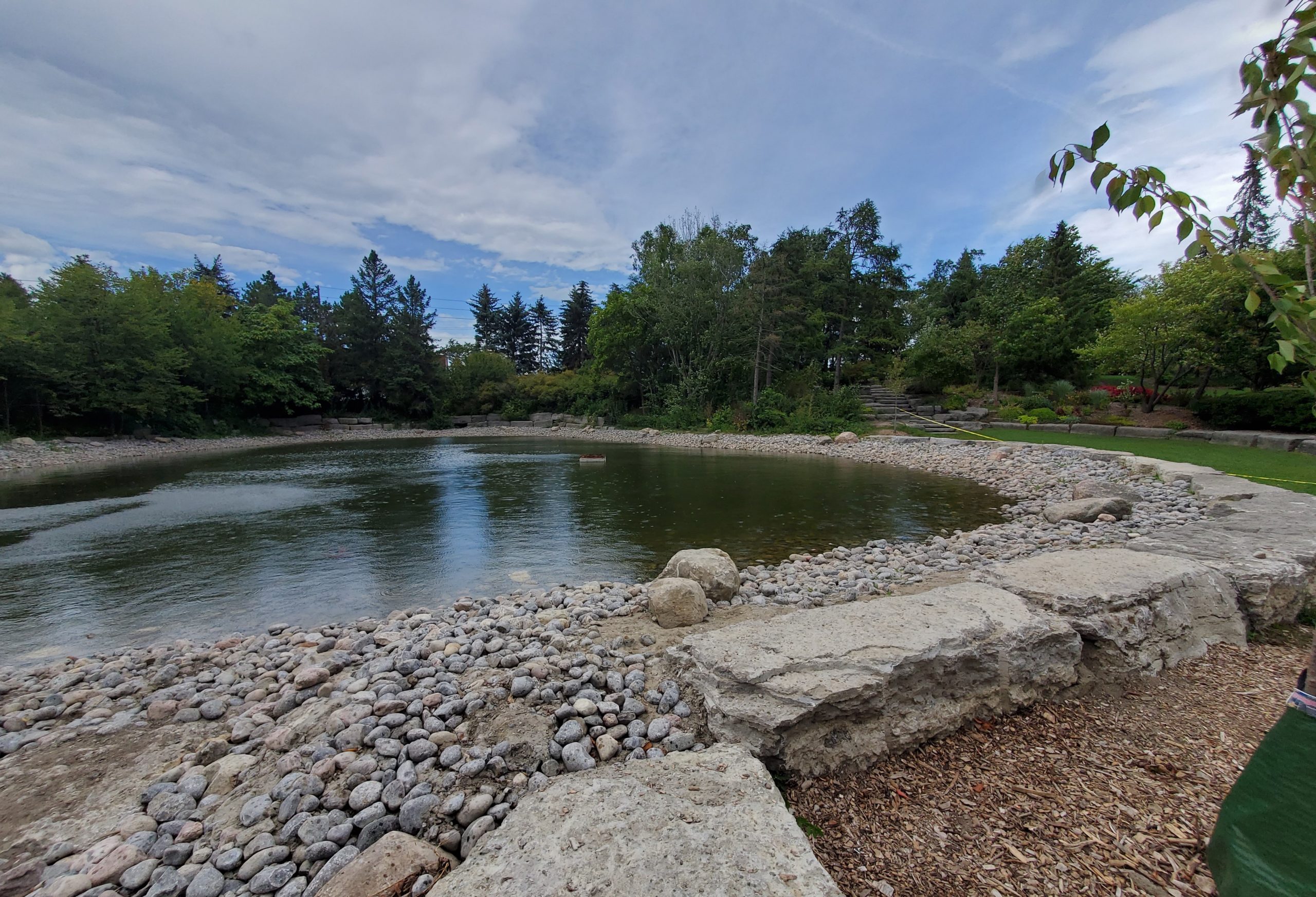 A photograph of the restored Pond A and stream, which occurred during Phase 2 construction. The photo is taken facing north towards Steeles Avenue East and shows a pond surrounded by mature trees and rocks.