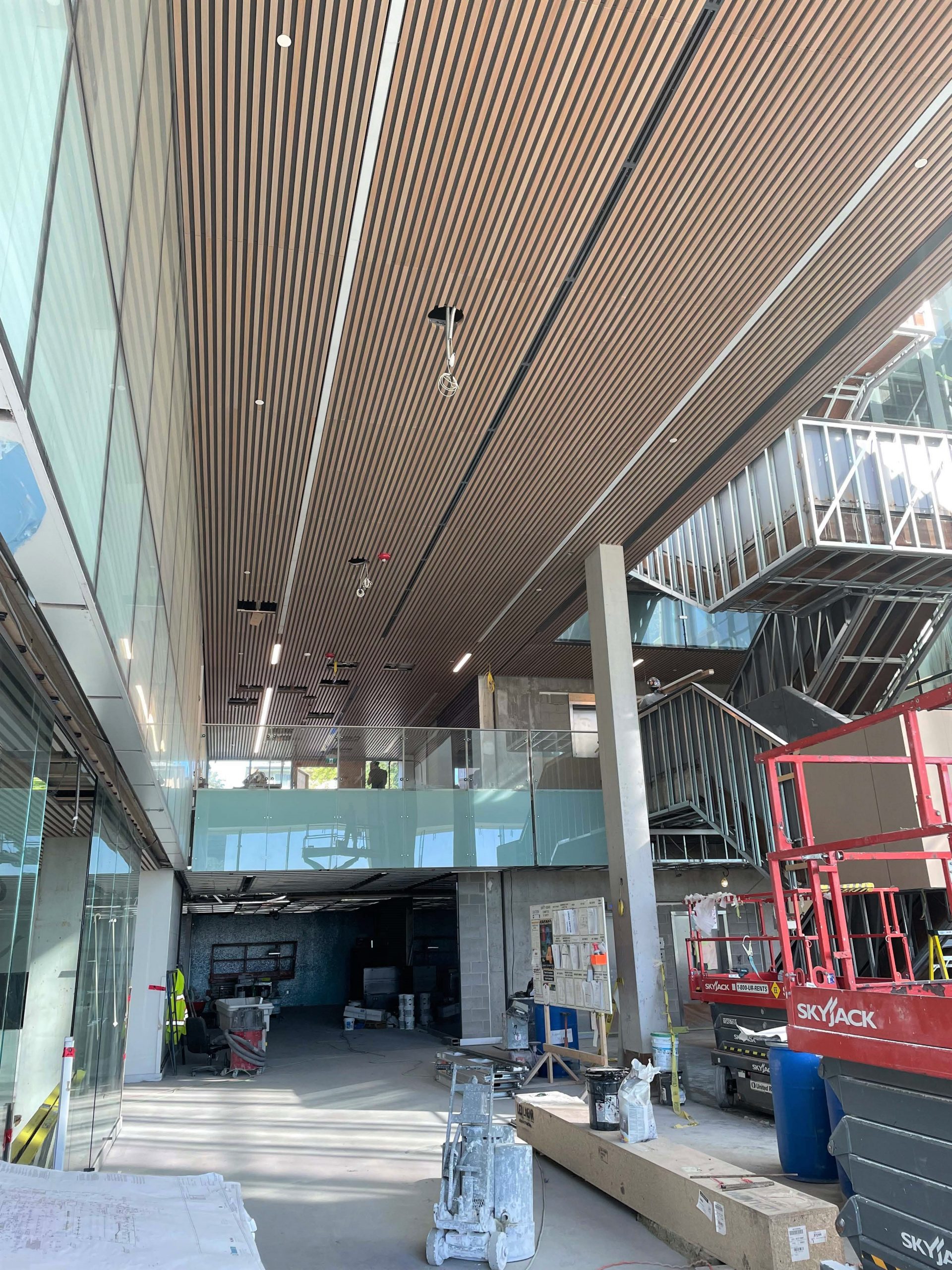 A photograph of the main gymnasium during construction, which shows partially installed basketball nets and an unfinished floor. The gymnasium is surrounded by glass walls which extend to the second floor running/walking track, which surrounds the gymnasium. 