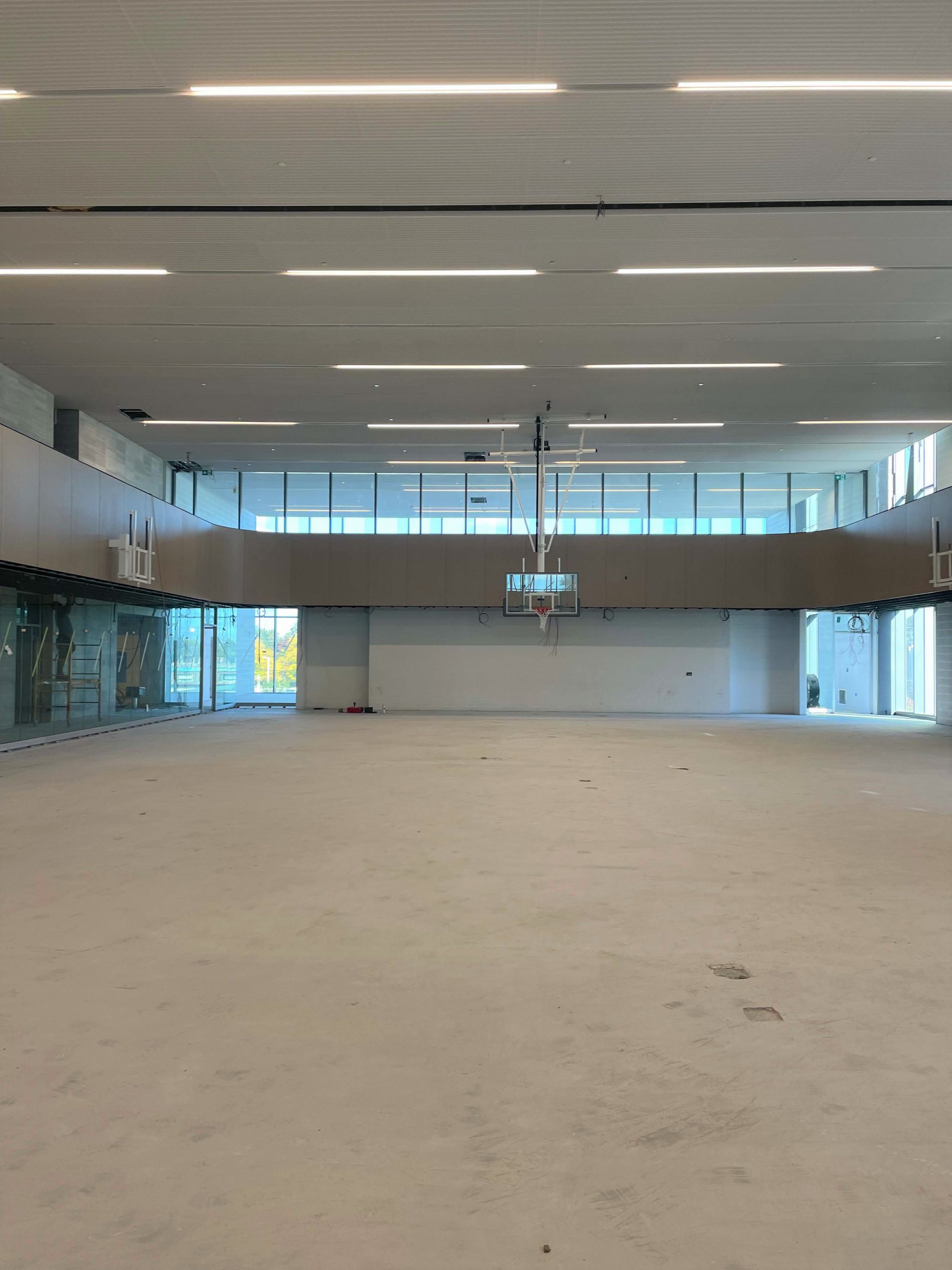 A photograph of the main entrance lobby during construction which shows a bright four storey space that includes a main feature staircase, main entrance to the library and reception desk for the aquatic facility. The linear wood ceiling is shown as being mostly installed, and addresses the acoustics for the space to minimize sound reverberation.