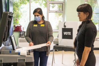 Polling station workers depositing ballet in ballet machine