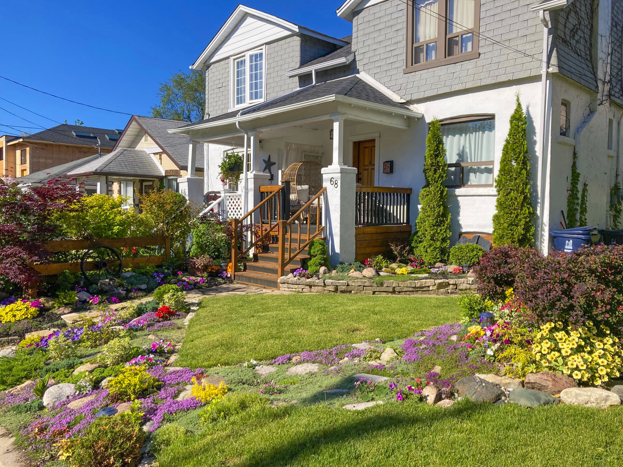 A front lawn garden in front of a house that has purple, yellow, green and red flowers.