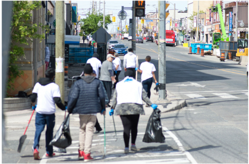 Group of people crossing an intersection carrying garbage bags and tools