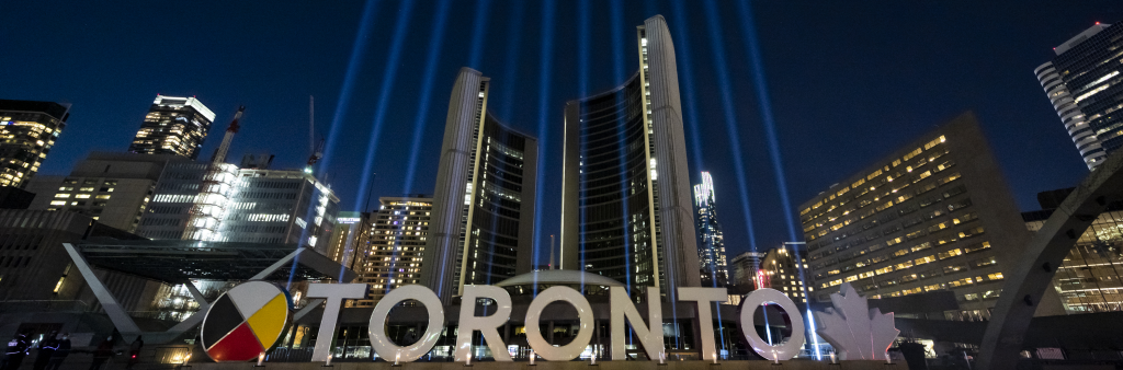 Vertical beams of light in front of City Hall towers. Toronto Sign in foreground.