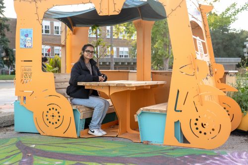 Woman sits at a picnic table set inside bus sculpture