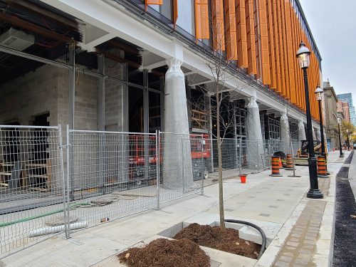 Exterior view of St. Lawrence Market, North Building from the street showing orange siding, construction cones and a fence.