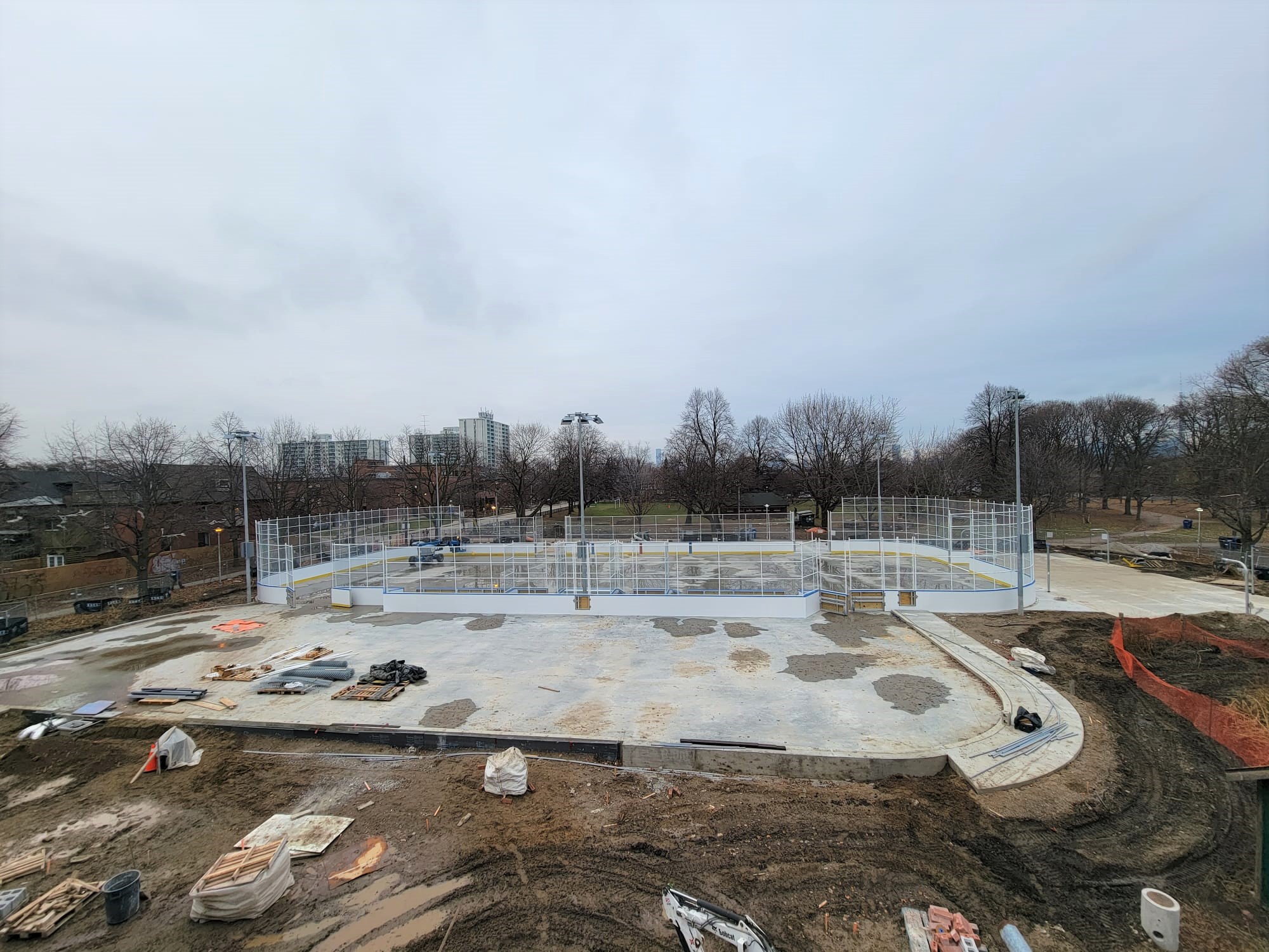 View of the hockey rink and leisure pad in Dufferin Grove Park taken from the roof of the Clubhouse looking east. It shows a construction site, with materials, new concrete and dirt. 