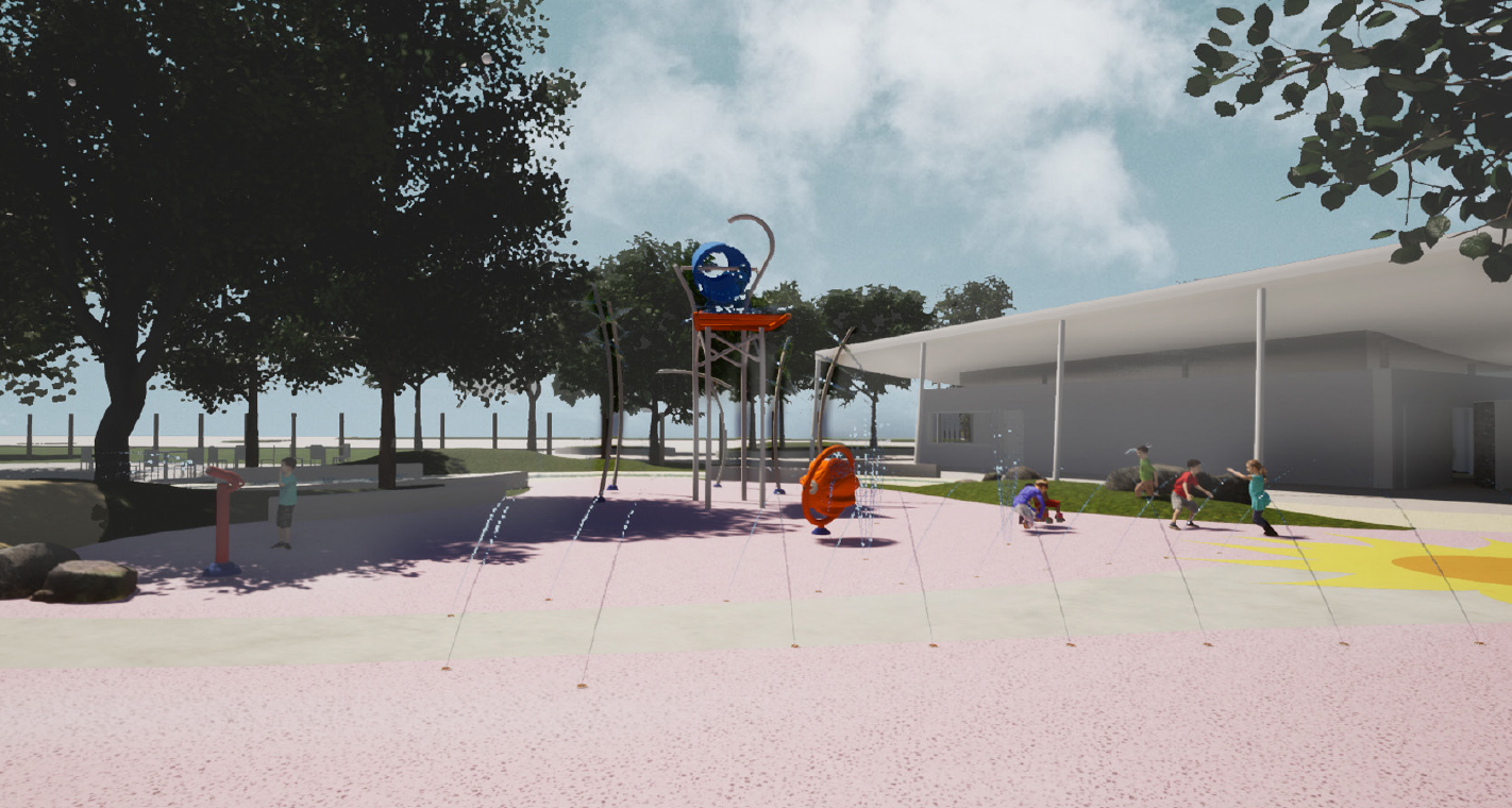 Rendering of the Senior Splashpad, with Bucket Dump, water room/spray tunnel, and other water play features that children are playing with. The Pavilion, which contains change rooms, washrooms, and offices, is on the right. There are trees and park fencing in the background on the left. This view is from the west-central part of the park looking north-west towards the entrance.